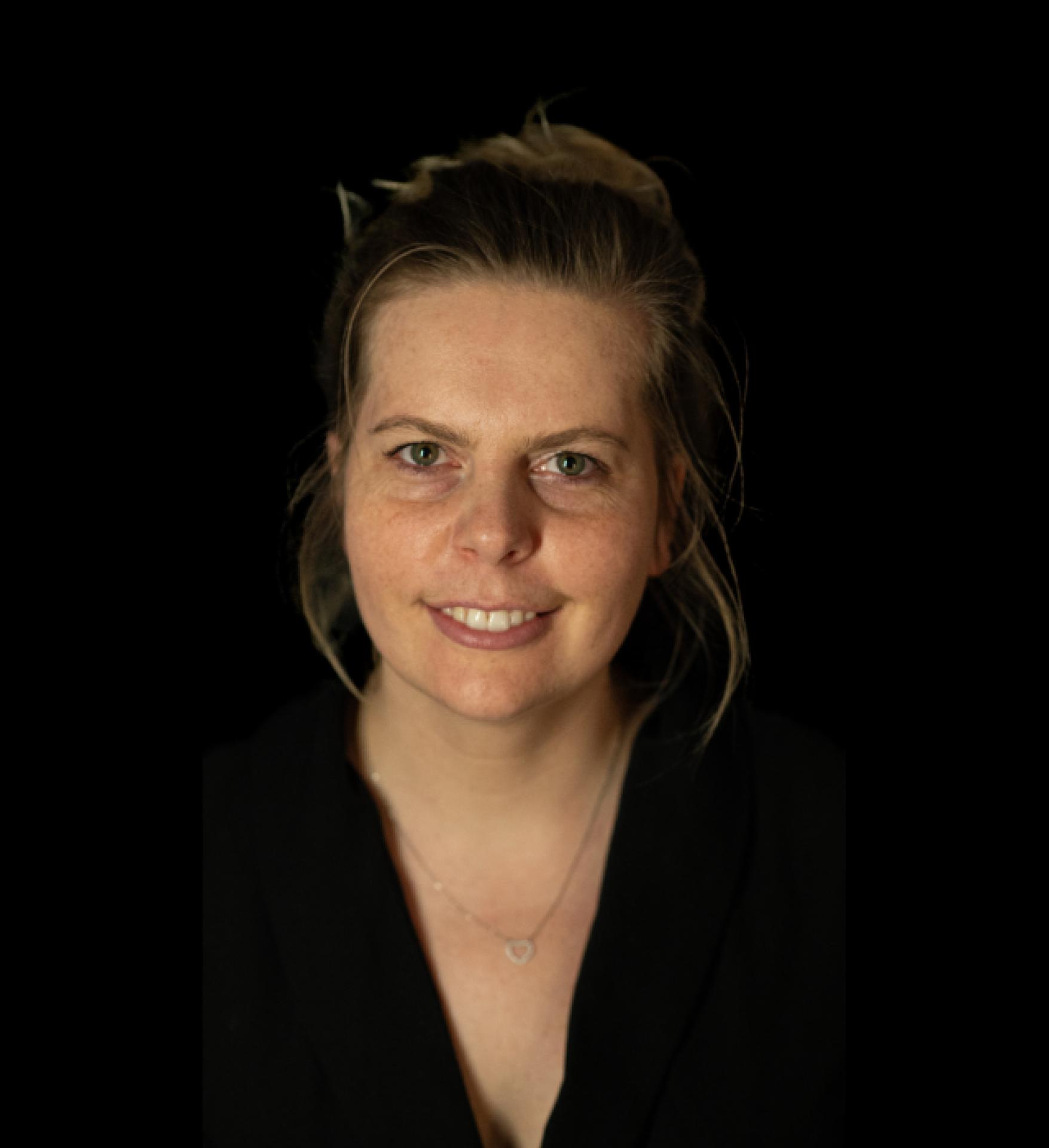 Alicja Bołdys - młoda uśmiechnięta kobieta ubrana na czarno, na czarnym tle. Włosy jasne blond, spięte.