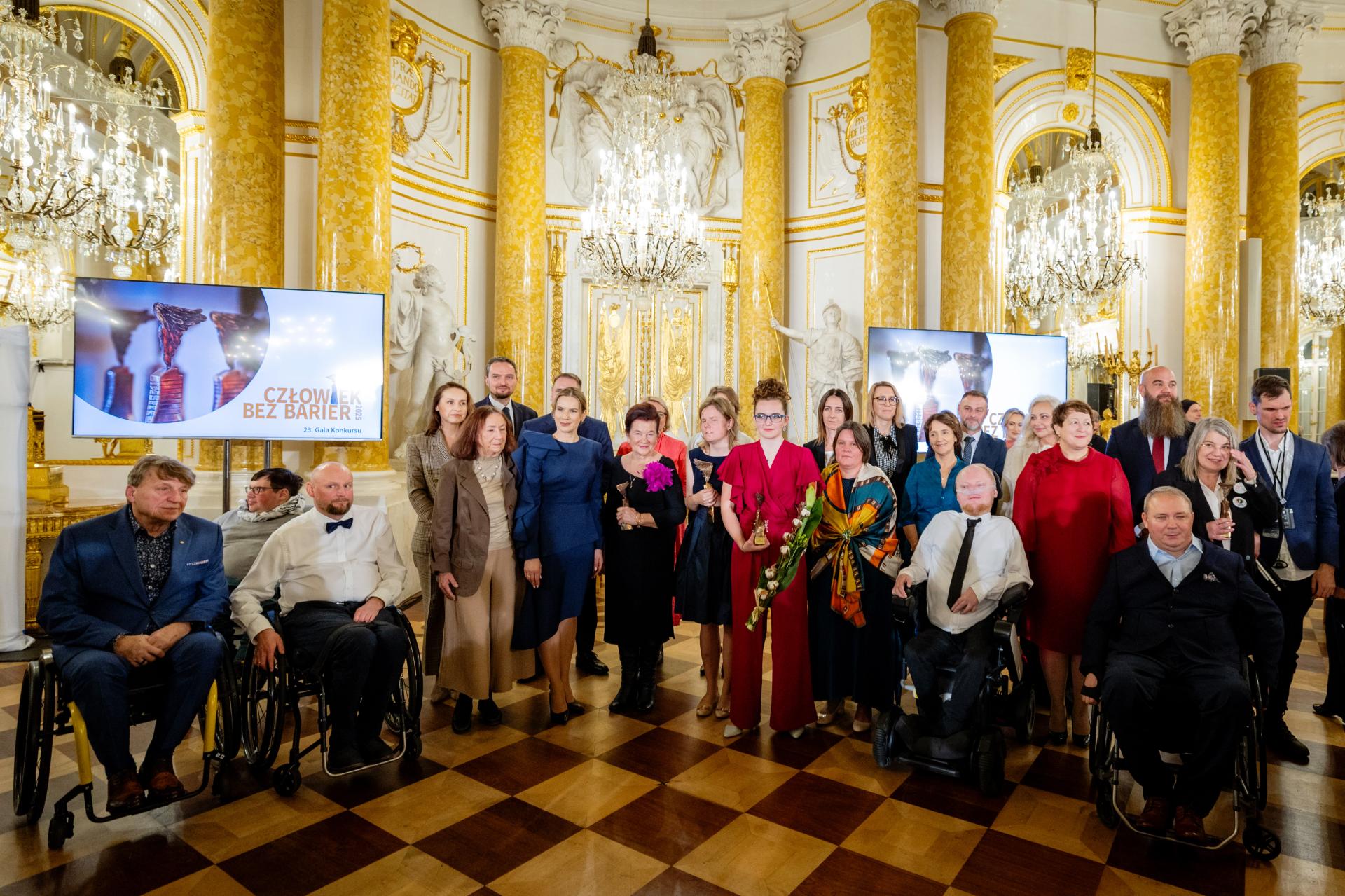 zdjęcie przedstawia grupę osób z sali wielkiej Zamku Królewskiego. Wśród nich stoi Pierwsza Dama